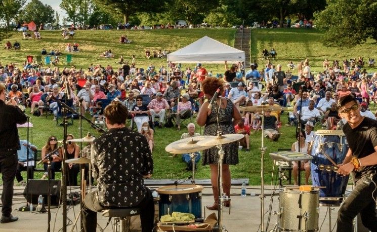 Musicians performing for a large crowd on a sloped lawn at a Levitt concert